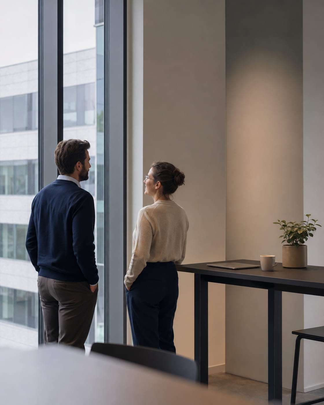 Two colleagues talking at a standing desk beside an office window.